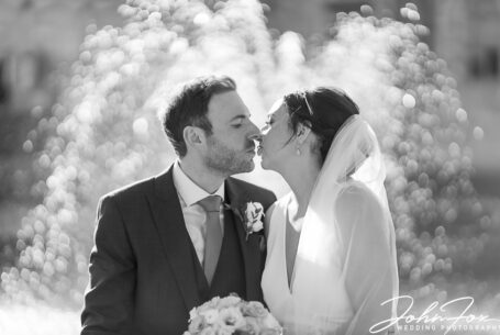 Nicole and Nicholas kissing by a fountain on their big day at Ashridge House, Hertfordshire