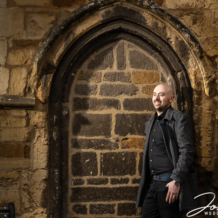 The groom, Samuel, standing by an ornate archway and wall