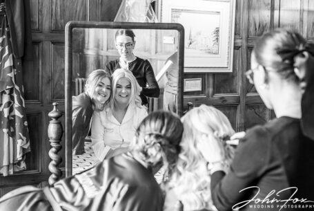 Bride and Bridemaids getting ready at Ashridge House and laughing together in a mirror.