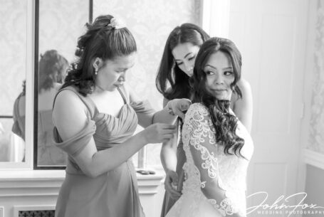 A bridesmaid helps the bride with her wedding dress. Photo by John Fox Wedding Photography