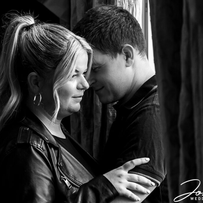 Black and white image by John Fox of the bride and groom-to-be sharing an intimate moment by a window in Ashridge House
