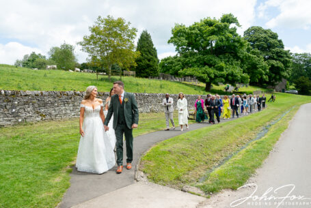 Iconic image at Tissington of bride and groom walking back from the church to the hall. Wedding Photography Derby.