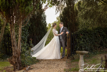 Bride and groom standing at the family farmhouse gate. Image by John Fox Wedding Photography.