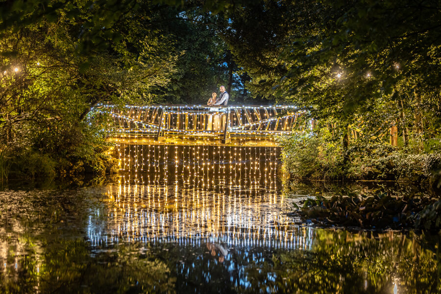 Evening photo of the happy couple on a beautifully lit bridge over the lake. John Fox Wedding Photography.
