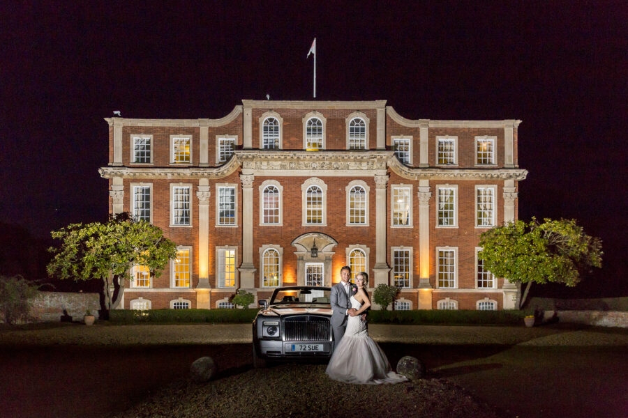 Night image of Chicheley Hall with Bride and Groom and the wedding car