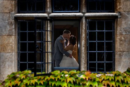 Bride and groom kiss with creative lighting from outside looking in by John Fox Wedding Photography