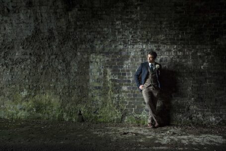 Posed image of the groom casually leaning against a wall
