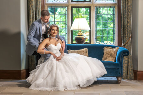 Posed style wedding image of bride and groom sitting on a sofa in a bay window