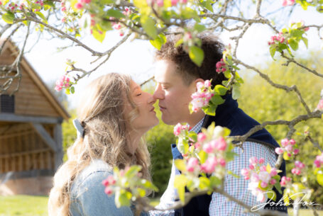 Kissing photo taken with apple blossom in the foreground in Oxfordshire