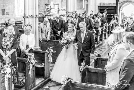 Wedding photography Wiltshire. Bride being walked down the aisle by her father at a church in Tisbury.
