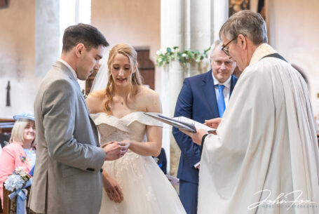 Image of bride and groom with the vicar exchanging wedding rings by John Fox Wedding Photography