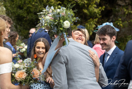 Wedding photography Wiltshire. Natural image of bride and groom with guests and bridesmaid hugging the groom