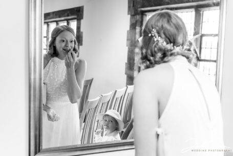 Bride checking her lipstick with flower girl looking on