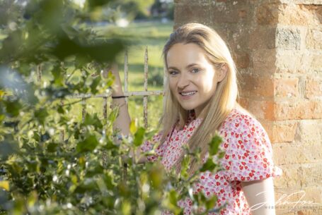 pre-wedding shoot image of the bride by a gate and framed by a holly bush at the Warwickshire family home