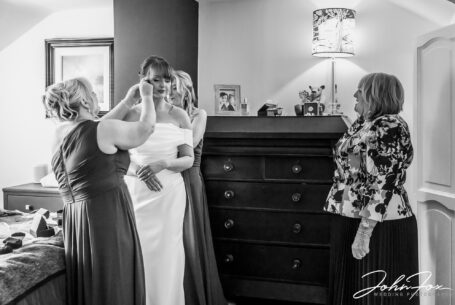 Bridesmaids assisting the bride getting ready with mum watching. Leicestershire wedding photography by John Fox.