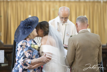 Brides mother kissing her daughter as she gives her away during church ceremony in Leicestershire