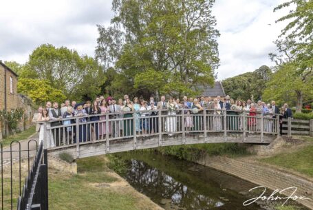 All the wedding guests group shot on a bride over a stream in Leicestershire