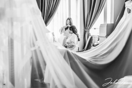 Bridesmaid helping bride put on necklace photographed through the wedding dress and veil.