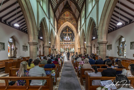 Wide image showing church interior and guests during a wedding ceremony. Wedding Photography in Gloucestershire