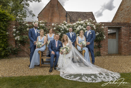 Formal group sitting on a bench with white roses in the background at Primrose Hill Farm
