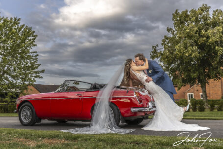 Bride and groom with the wedding car. Kissing on the back of car