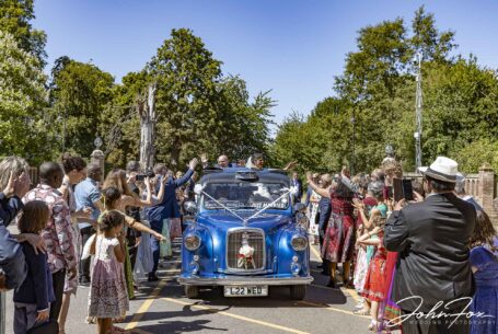 Bride and groom standing up in wedding car driving by the excited wedding guests in Bedfordshire