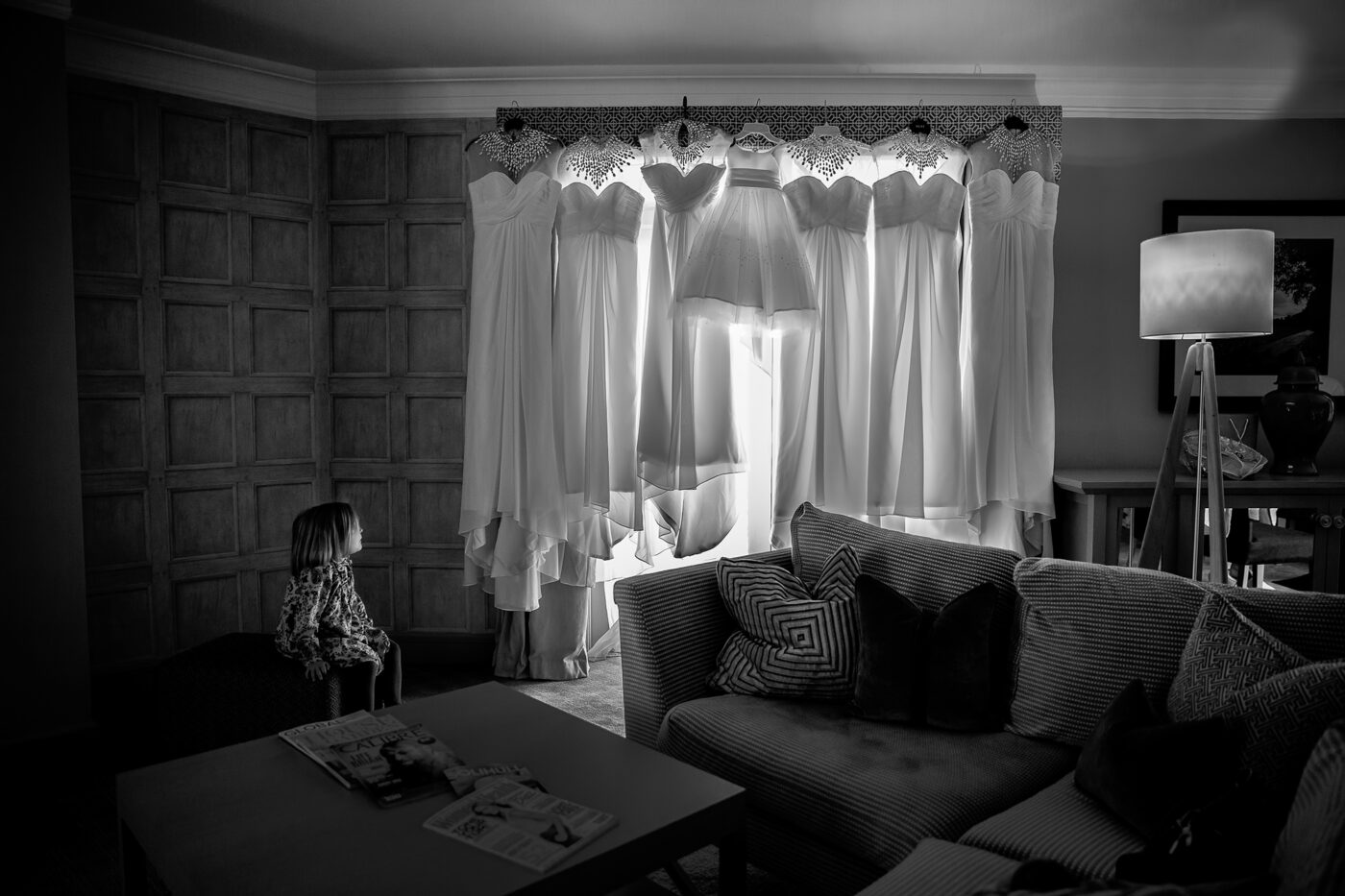 A flower girl sitting, looking at her dress hung in a window alongside the bride's and bridesmaid's dresses. Help Planning Your Wedding Hints, Tips and Advice by John Fox.