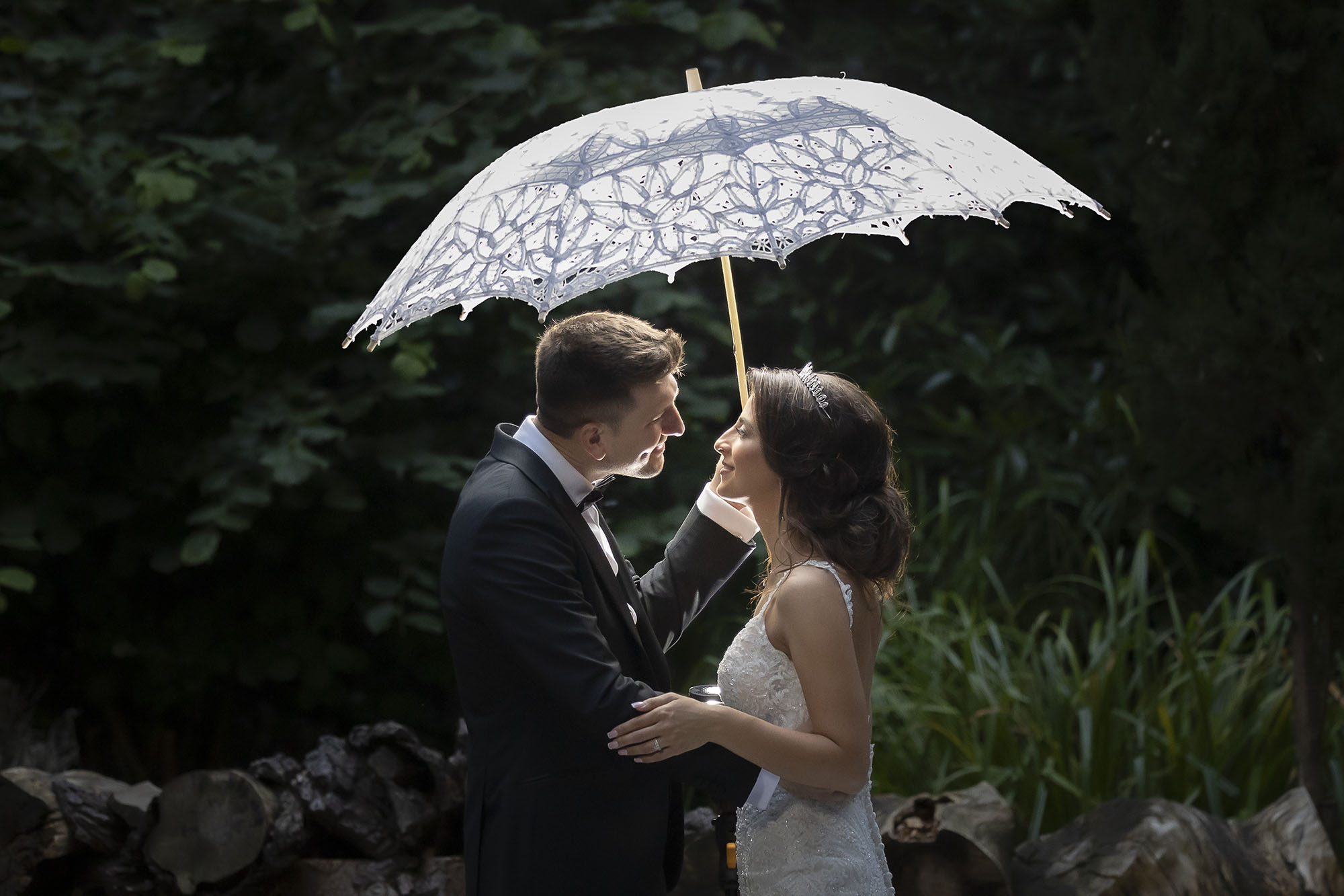 A newly-wedded couple about to kiss under an umbrella.