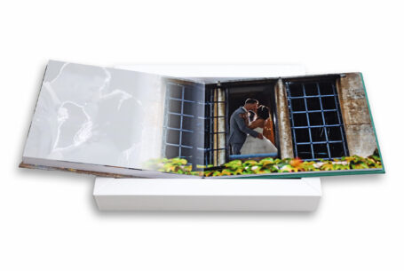 Help Planning Your Wedding Hints Tips and Advice – Part 11 - A wedding album created by John Fox Wedding Photography opened at an image of the newly-weds kissing at a window with flower beds in the foreground.