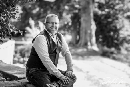 Groom to be Kevin on his pre-wedding shoot sitting on a wall at Rushton Hall in Northamptonshire