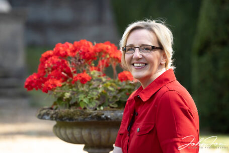 Bride to be Joanne on her pre-wedding shoot in a red dress captured between red flowers at Rushton Hall in Northamptonshire
