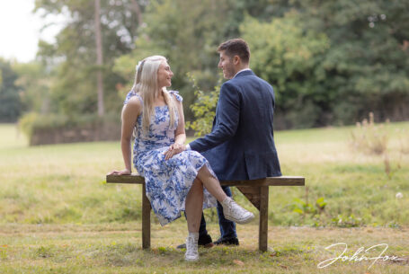 Couple on a pre-wedding shoot in Kilworth House gardens sitting on a bench overlooking fields