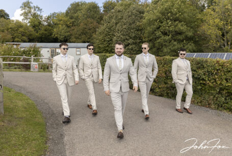 Groomsmen all together walking to the wedding venue at Kingscote Barn in Gloucestershire.