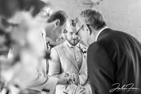 Groom and best man with registrar checking the wedding rings at Kingscote Barn, Tetbury