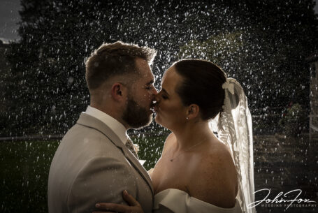 Bride and groom kissing in the rain at Kingscote Barn in the Cotswolds