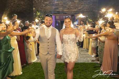 Family and friends gathering outside with sparklers at Gabrielle and William's Kingscote Barn wedding in Tetbury, Gloucestershire