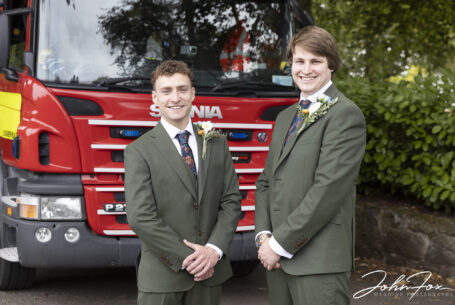 The groom and best man standing in front of the fire engine.