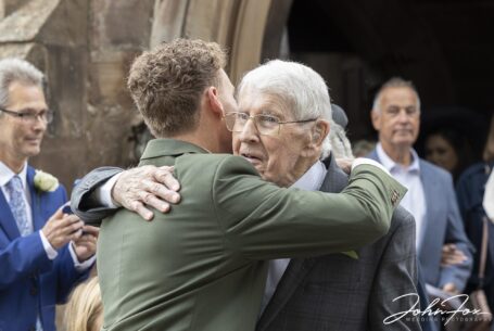 The groom Lewis getting a hug from one of the wedding guests outside Ashley St John the Baptist Church.