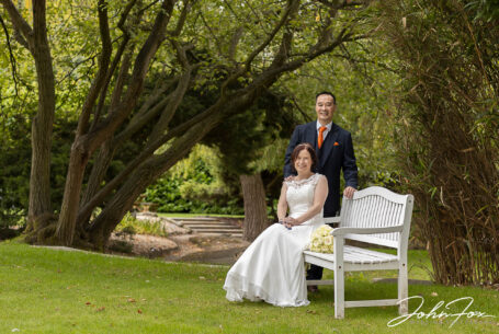 Bride and groom portrait using a bench and gardens to make the setting at Hadley Park House. Image by John Fox Wedding Photography.