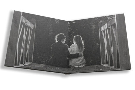 Sophie and Jack sitting on the steps of a wooden bridge at Hothorpe Hall The Woodlands. This black and white image is part of their unique personalised guest book from John Fox Wedding Photography.
