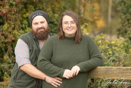 The bride and groom to be leaning on a fence at their farm. Northamptonshire wedding photographer John Fox