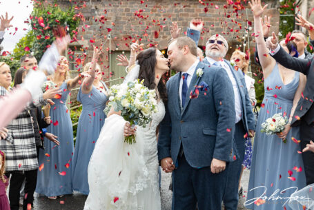 Bride and groom with guests throwing confetti outside the West Barn at The Ashes Barns in Staffordshire