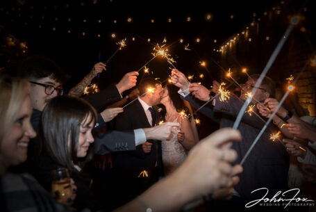 Bride and groom through an arch of sparklers being held by their guests at The Ashes Barns in Staffordshire