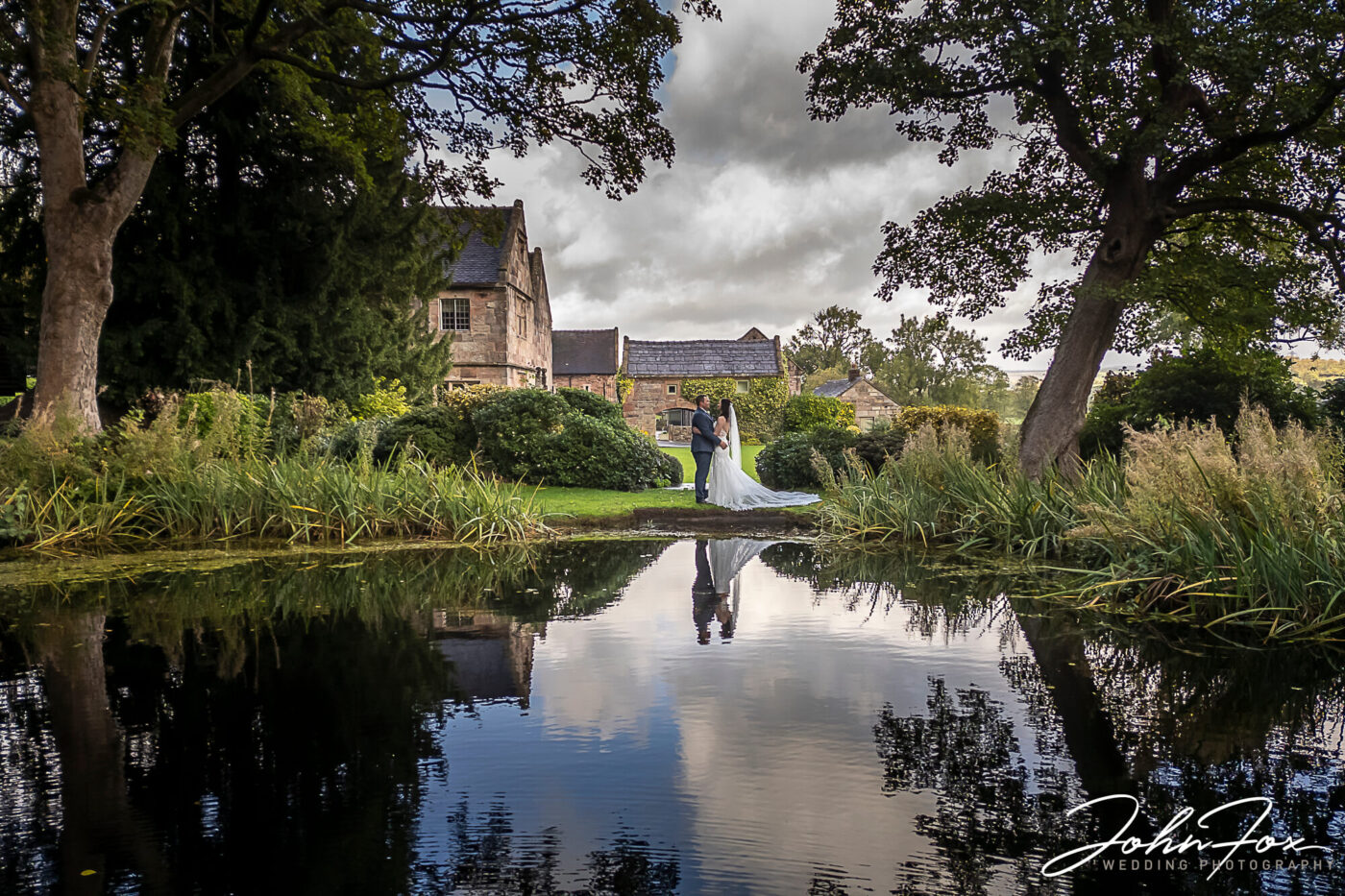 Wedding Photography at The Ashes Barns in Staffordshire. The newly-weds reflected in the lake in the grounds