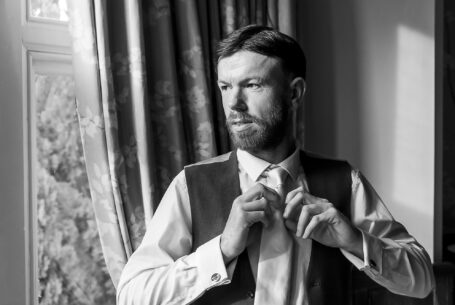 Black and White image of Shane tying his tie in preparation for the wedding ceremony at Holmewood Hall