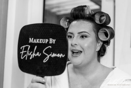 Abigail looking in a mirror and loving her make-up. Northamptonshire wedding supplier, John Fox.