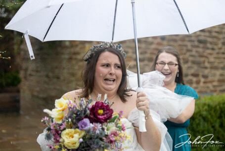 Abigail, the bride, hanging on to an umbrella on her wedding day at Dodford Manor, Northamptonshire.
