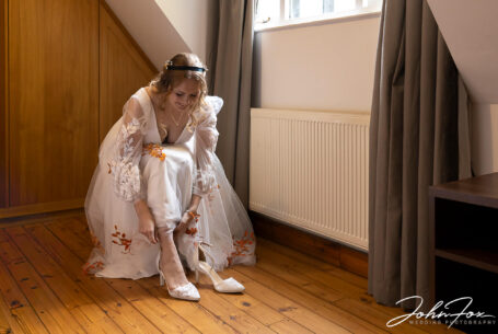 Sophie, the bride, putting on her wedding shoes for her special day at Hothorpe Hall, Northamptonshire