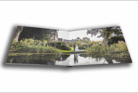 Joanne and James reflected in a lake in the grounds at The Ashes Barns in Staffordshire. Wedding album double-page image by John Fox.