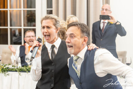 A singing waitress at Rushton Hall dancing with a wedding guest. Wedding packages in Northamptonshire from John Fox Wedding Photography.